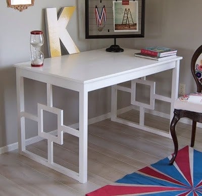 An IKEA Ingo desk in a room has been upgraded with decorative legs and painted white using DIY IKEA hacks. A giant "K" sits on the desk along with other office paraphernalia. 