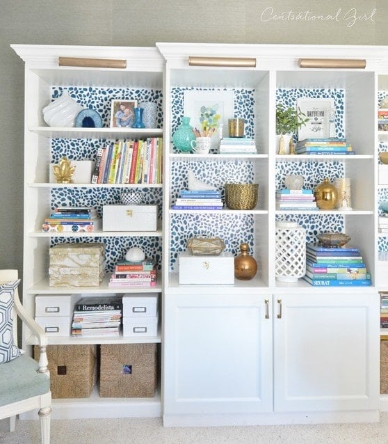 Besta and Billy bookcases from IKEA include lower cabinet doors and gold light fixtures on the top. Behind the books and knickknacks on the shelves is a graphic polka-dot backing. 