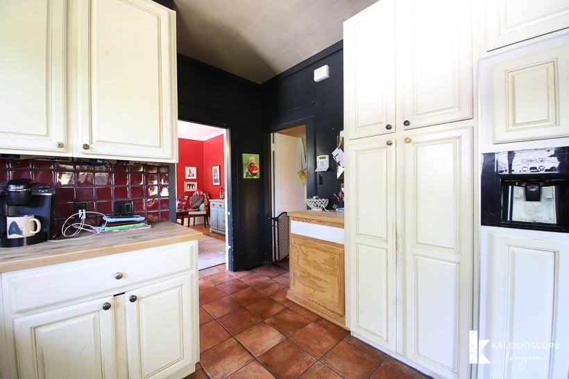 A different view of the back half of an outdated kitchen before budget-friendly kitchen makeover shows white cabinets, dark walls, and a narrow entry.
