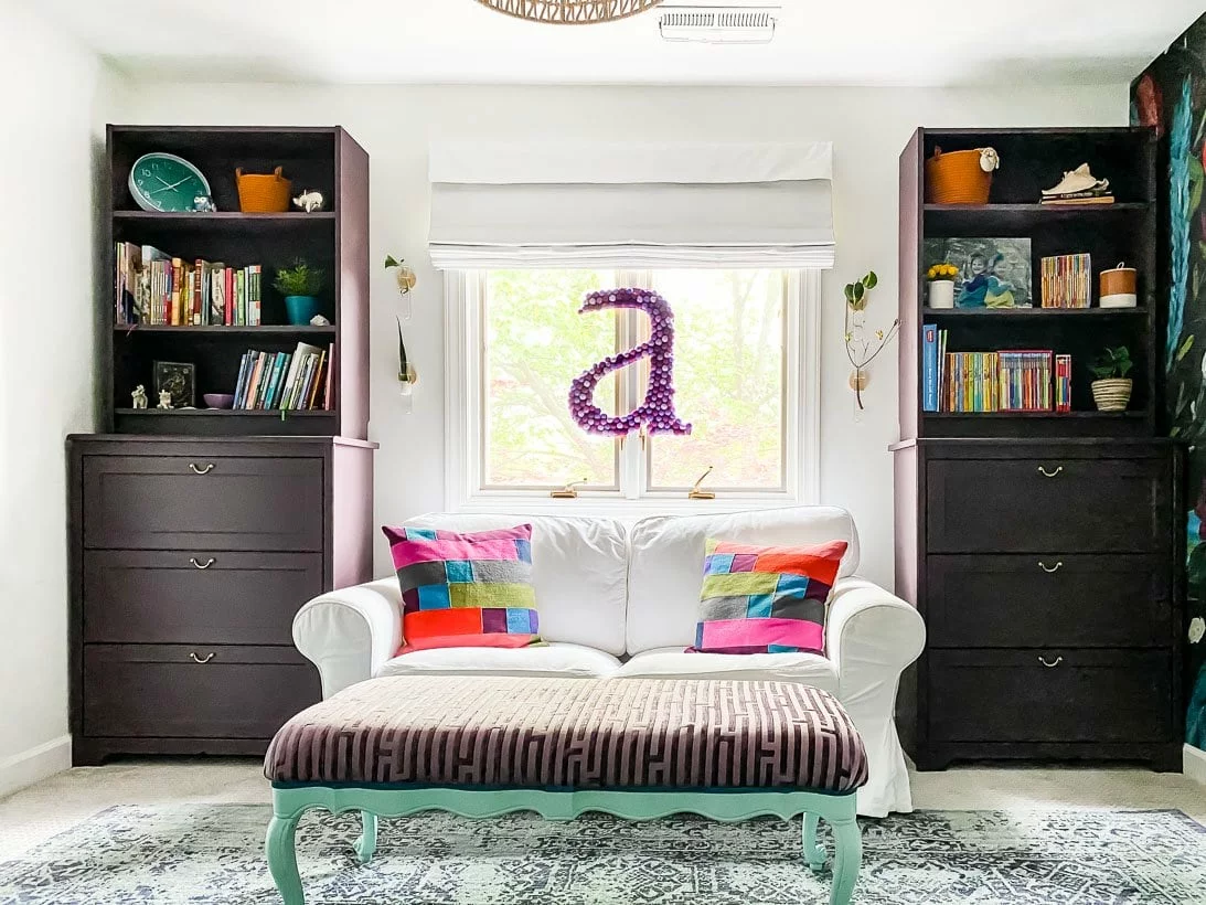 A quaint room featuring a white couch and two IKEA Billy bookcase on either side of the window. 