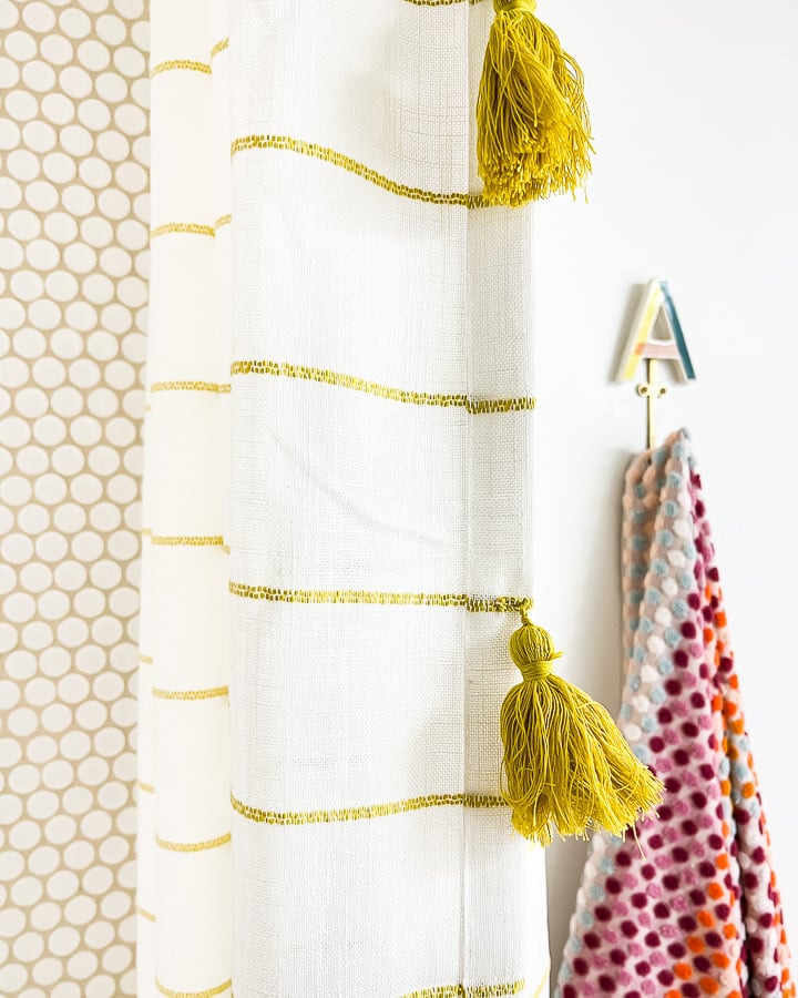 Round tiles in the shower with white and gold curtains with gold tassels next to a fun towel hook with the letter "A" on top. 