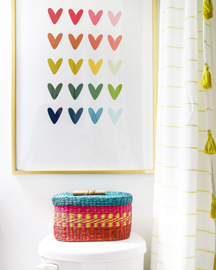 No bathroom makeover on a budget is complete without colorful artwork like rainbow heart artwork and a rainbow toilet paper basket. 