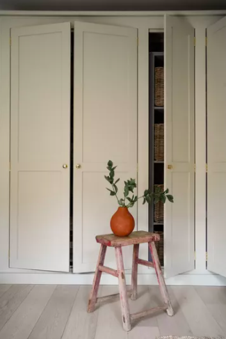 White built-in wall storage from Billy bookcases line the walls. The doors are slightly ajar. A step ladder with a plant on it sits in front of this DIY IKEA hack. 