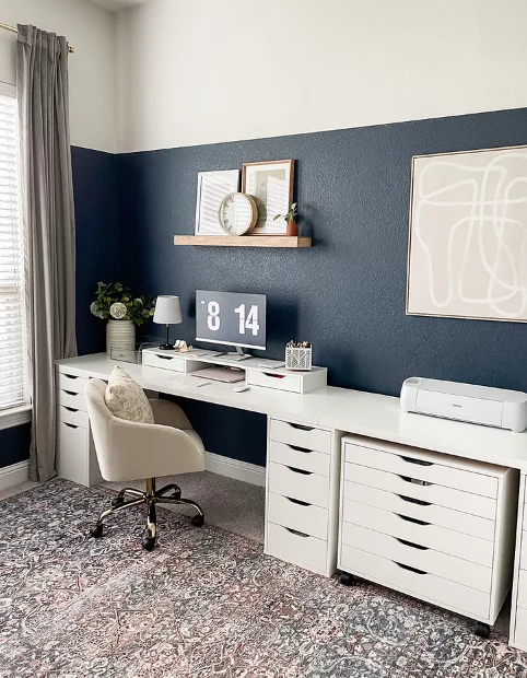 IKEA desk setup for office craft room includes a long white countertop, plenty of drawers underneath, a blue color block wall and space for a Cricut machine. 