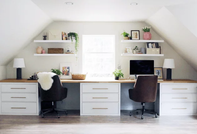 IKEA desk hack with open shelving and leather desk chairs under an angled attic roof. A long countertop on top of IKEA drawers creates two desks with separate workstations. 