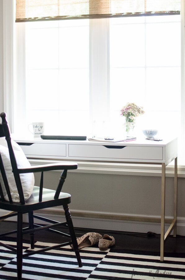 A slim white desk with two under-mounted drawers provides a work area that takes up little space. A wooden black chair and slippers on a black and white rug complete this IKEA desk hack. 