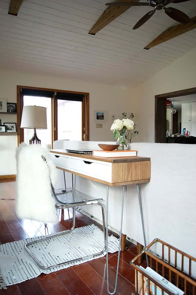 A large living room with a slim IKEA desk behind the white couch. The high ceilings and fan highlight the minimalist room.  