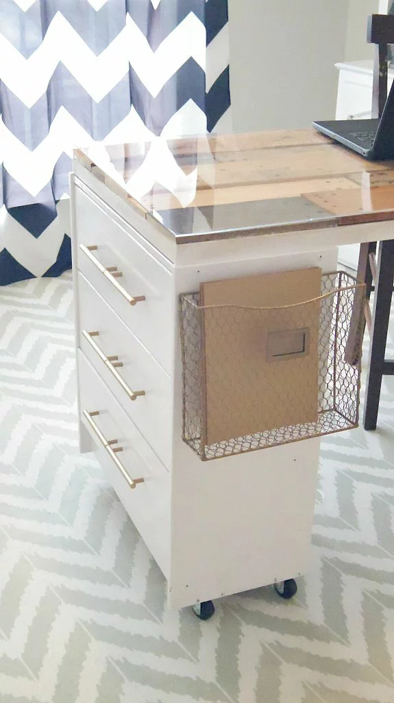 A glass top on a wooden desk made from IKEA drawers against a blue and white chevron curtain. 