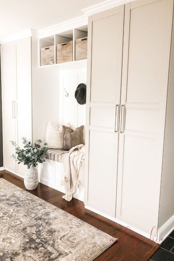 Two IKEA Pax wardrobes are separated by a DIY bench to create a mudroom along a wall in a living room. 