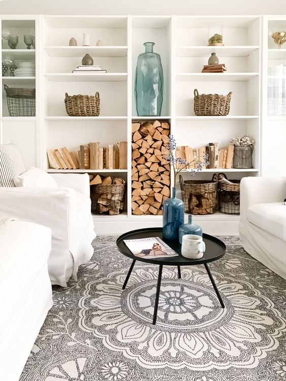 A white family room with white couches features IKEA Billy bookcases customized as built-ins along the back wall, with shelves full of art, wood, books, and more. 