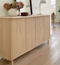 A hallway has an IKEA Ekat sideboard cabinet piece covered in pole wrap, with legs added and a table top with flowers, a mirror and a lamp.