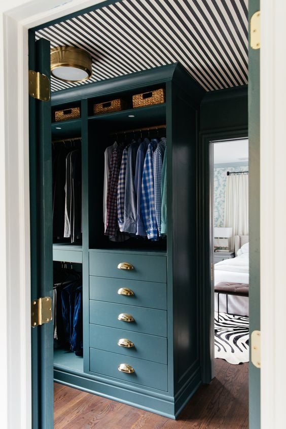 A dark green custom closet is made from DIY IKEA hacks using Pax shelves and drawers. The shelves have hanging clothes above deep drawers on the bottom. 