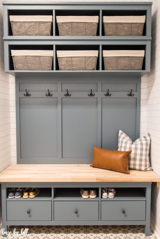 A grey mudroom bench made with IKEA Hemnes drawers and cubbies and butcher block top. Two pillows sit on the bench and fabric bins line the shelves in this DIY IKEA hack. 