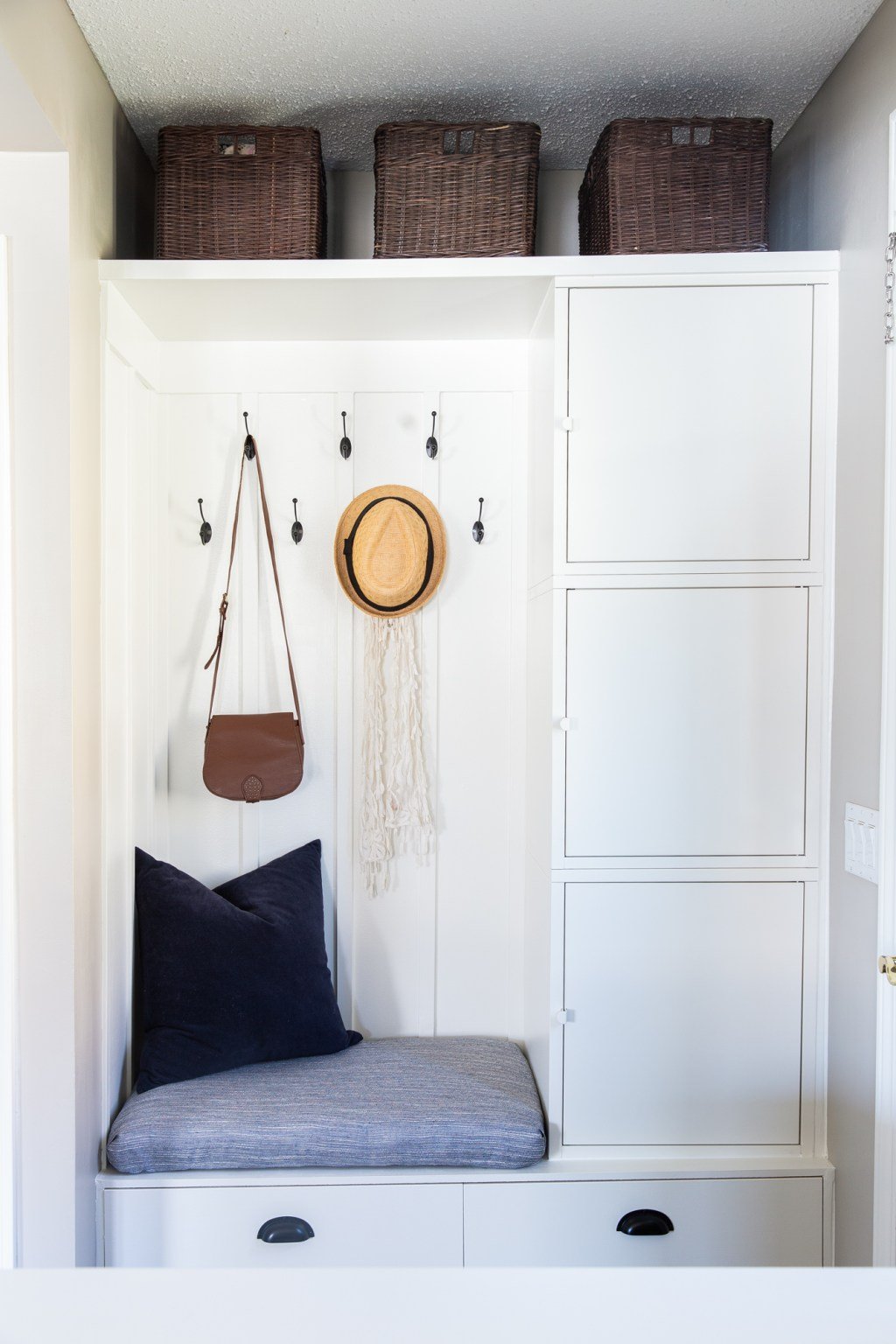 This DIY IKEA hack uses Besta and Hallan units to create a bench and cabinets along the side wall. Bins line the top shelf, while hooks behind the bench hold a hat and purse. 