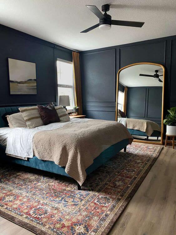 A bedroom with a giant gold mirror and bed has dark walls using blue gray paint colors. 