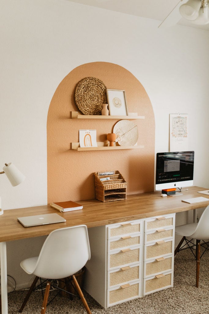 IKEA desk hack with caned drawers and arch mural above a long wooden desktop and shelves. 