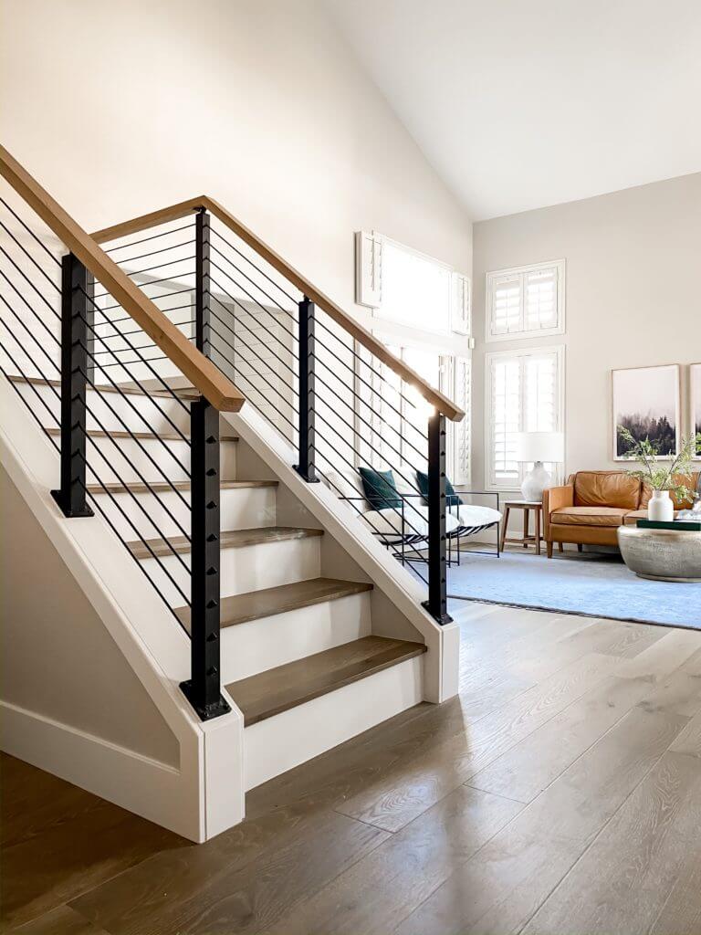 A metal black cable railing freshens white and wood stairs opening into a living room.