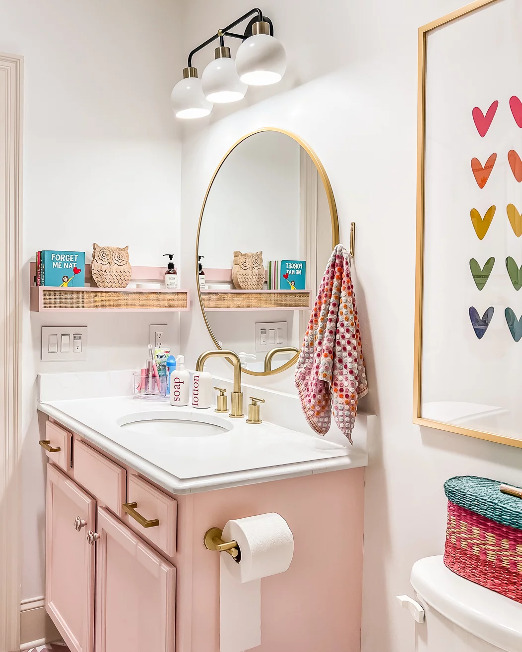 A teen girl's colorful pink and white bathroom makeover on a budget "after" photo includes a light pink sink cabinet, painted marble countertops, and white walls. 