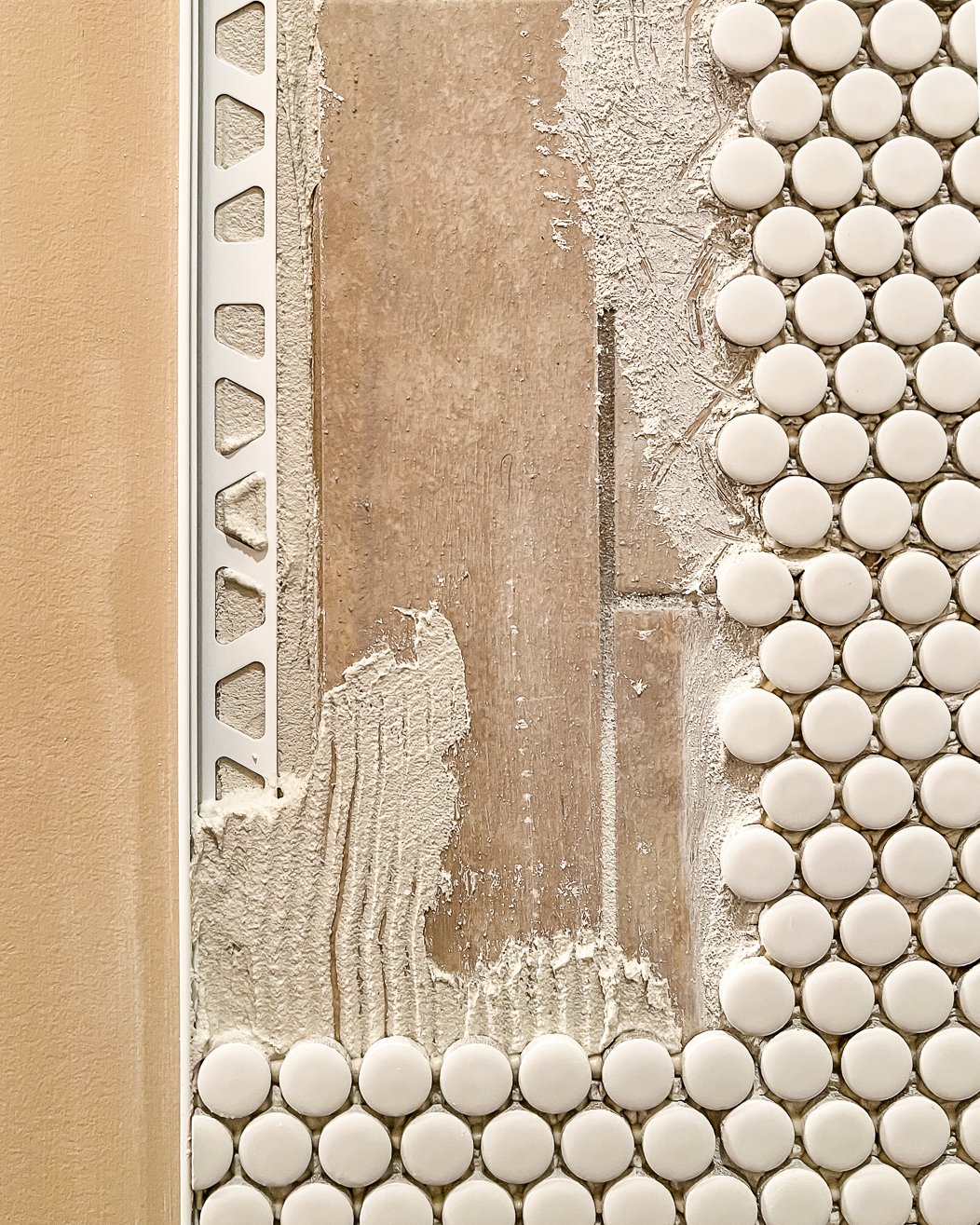 A close-up of small round tile being adhered to a bathroom wall over existing brown tile. This is one way to do a bathroom makeover on a budget.